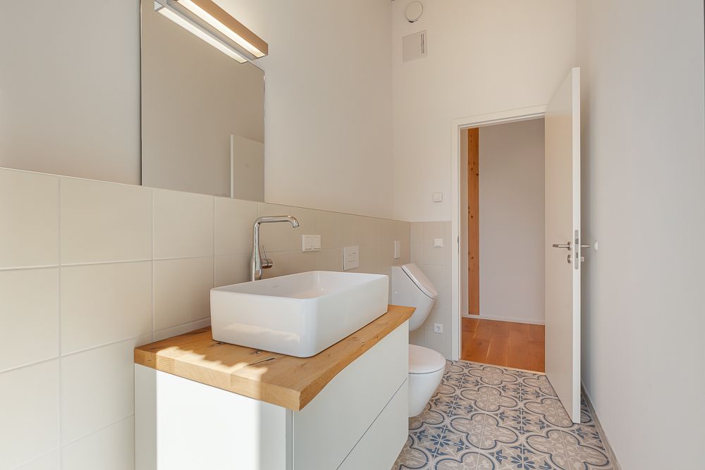 Modernes Bad mit Waschbecken, Spiegel, Toilette und gemustertem Fliesenboden.