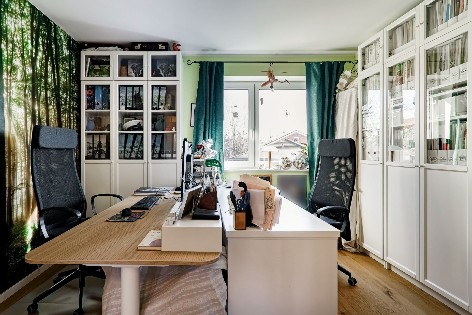 Helles Arbeitszimmer mit zwei Schreibtischen, Regalen, Bürostühlen und großem Fenster.