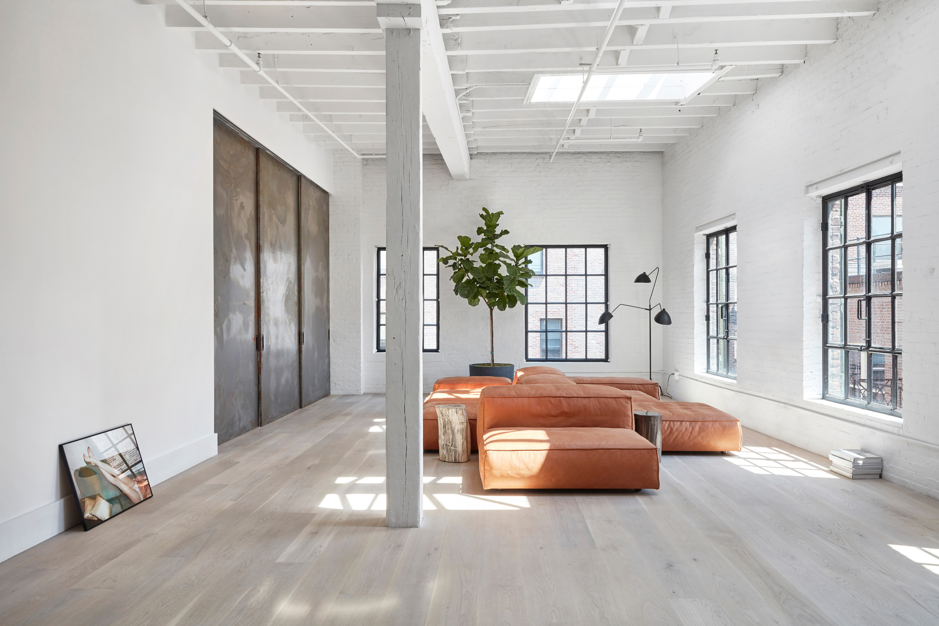 Helles Wohnzimmer mit großen Fenstern, orangen Sofas, Pflanze und Holzboden.
