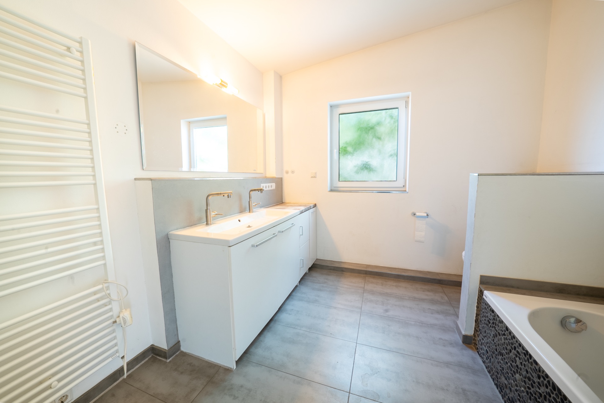 Modernes Badezimmer mit Doppelwaschbecken, Spiegel, Fenster und Badewanne.