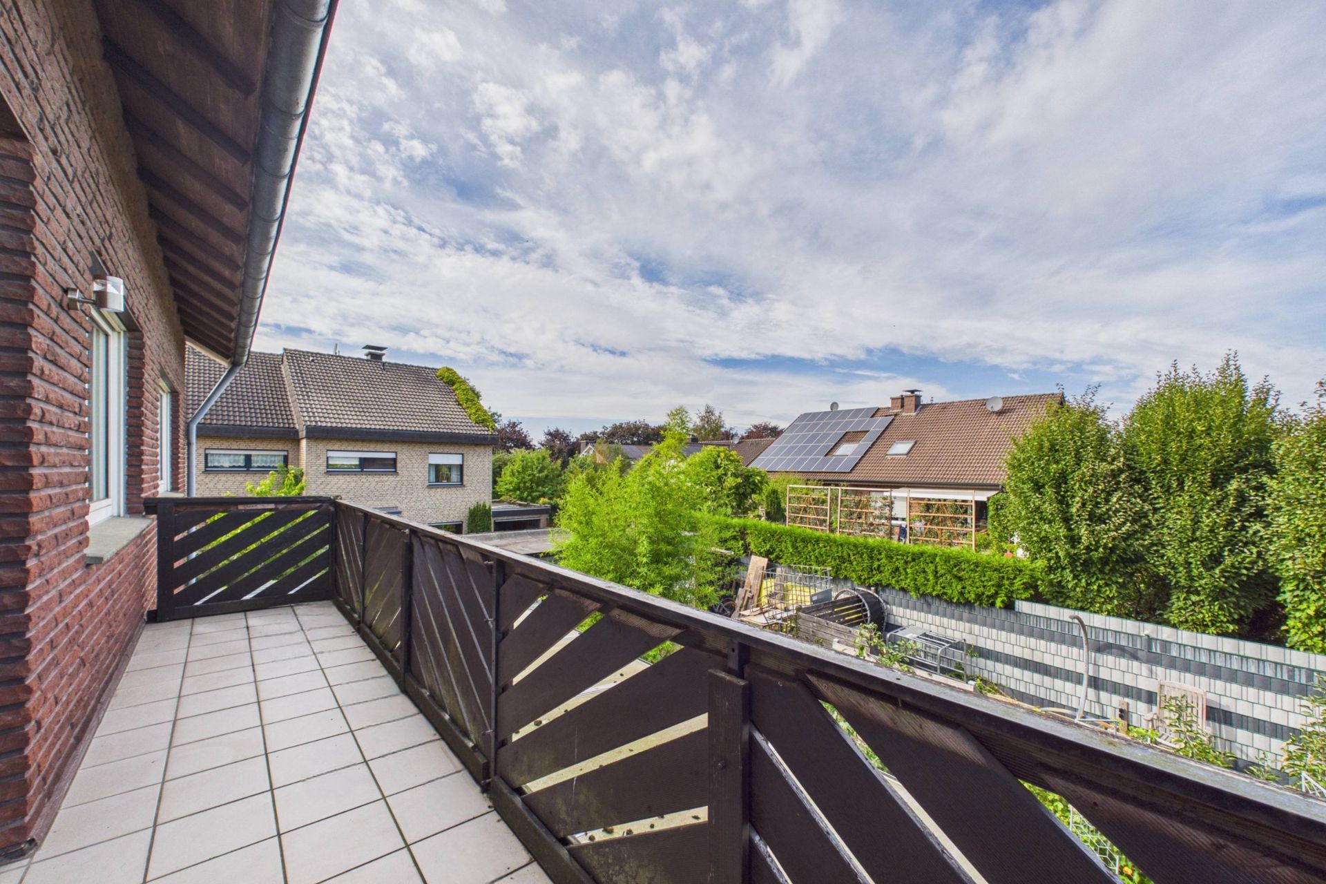 Balkon mit Fliesenboden und Blick auf Nachbarhäuser und Gärten bei Tageslicht.
