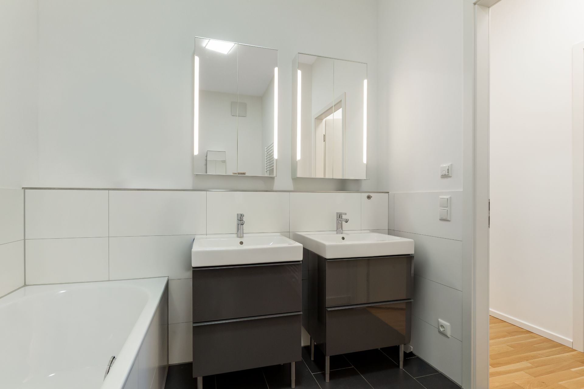 Modernes Bad mit zwei Waschbecken, beleuchteten Spiegeln und Badewanne.