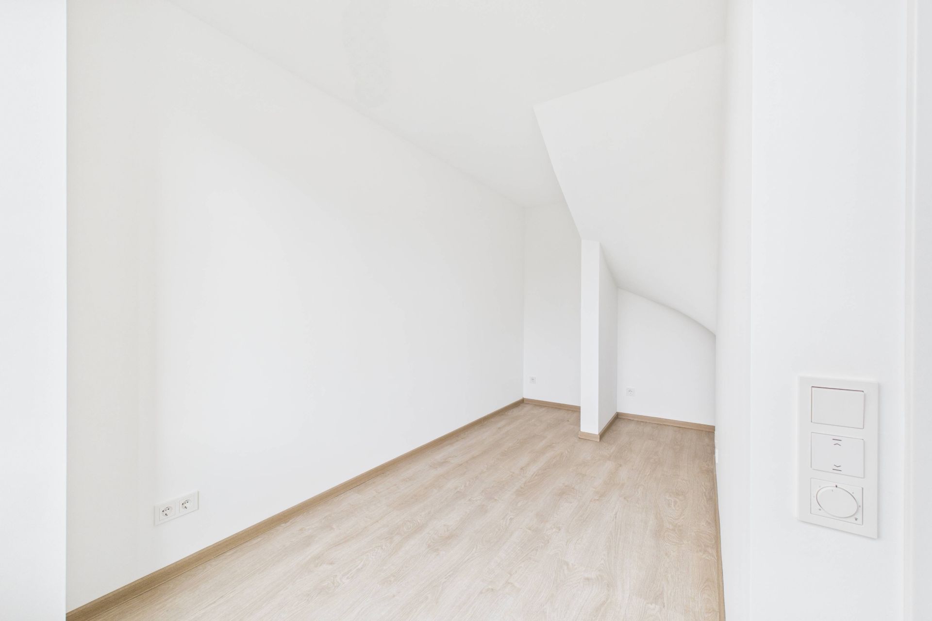 Heller, leerer Raum mit weißen Wänden und hellem Holzboden.