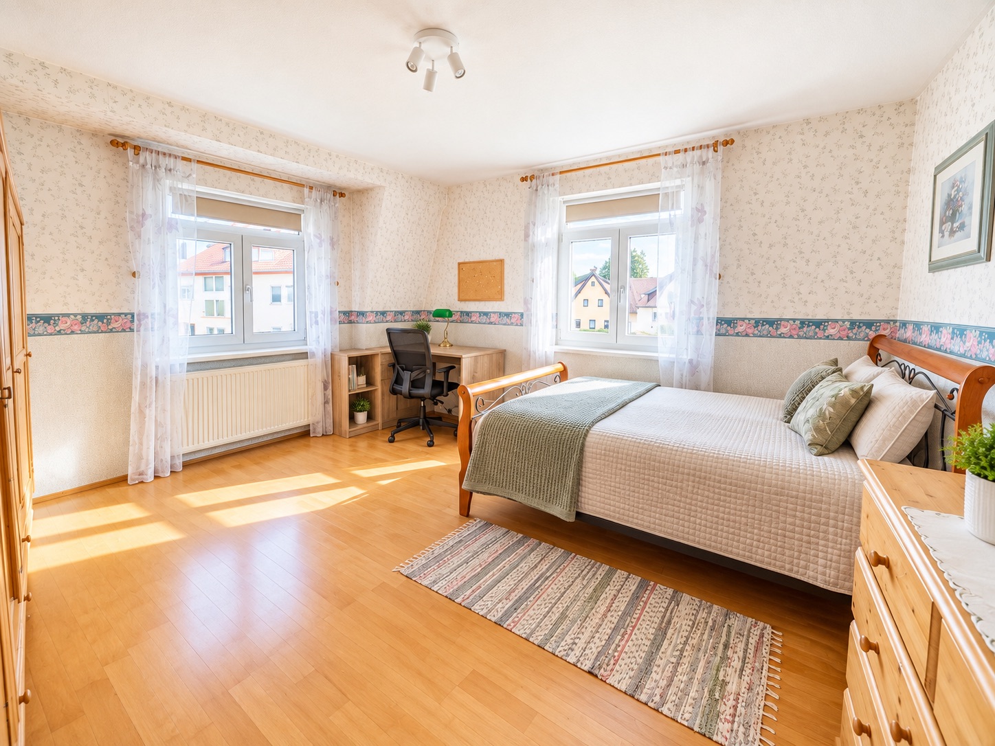 Helles Schlafzimmer mit Doppelbett, Schreibtisch, Stuhl, zwei Fenstern und Holzfußboden.