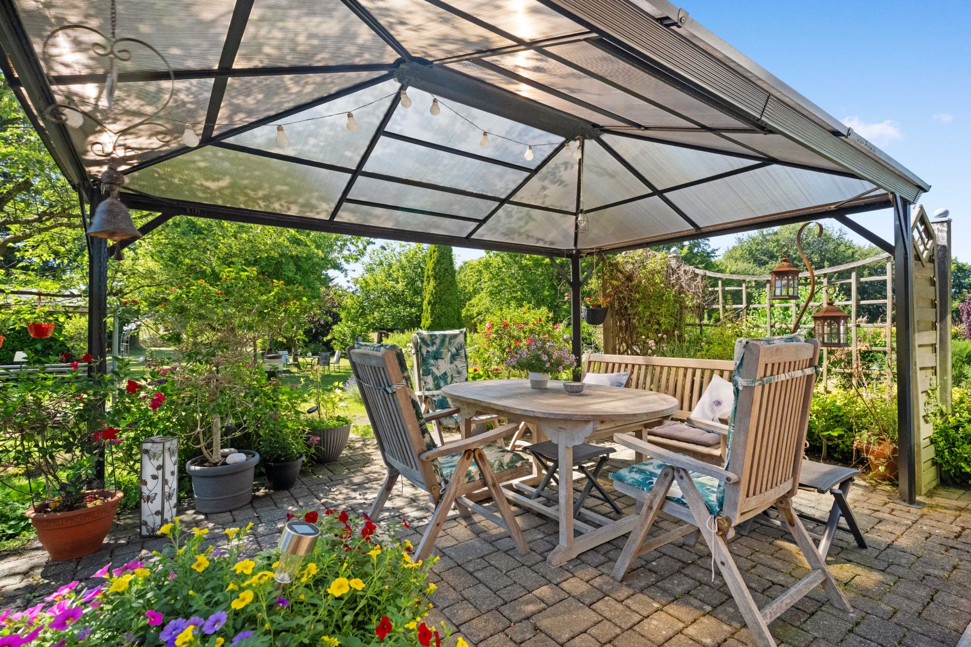 Überdachte Terrasse mit Holztisch, Stühlen und vielen Pflanzen im Garten.