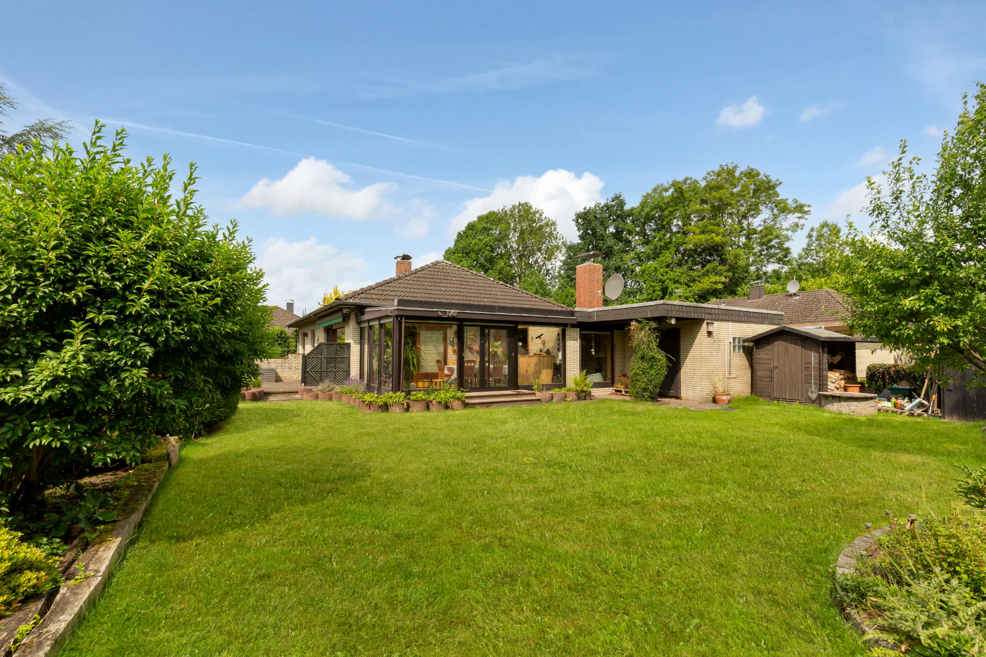 Einfamilienhaus mit großem Garten und Glasfront, umgeben von Bäumen und Rasen.