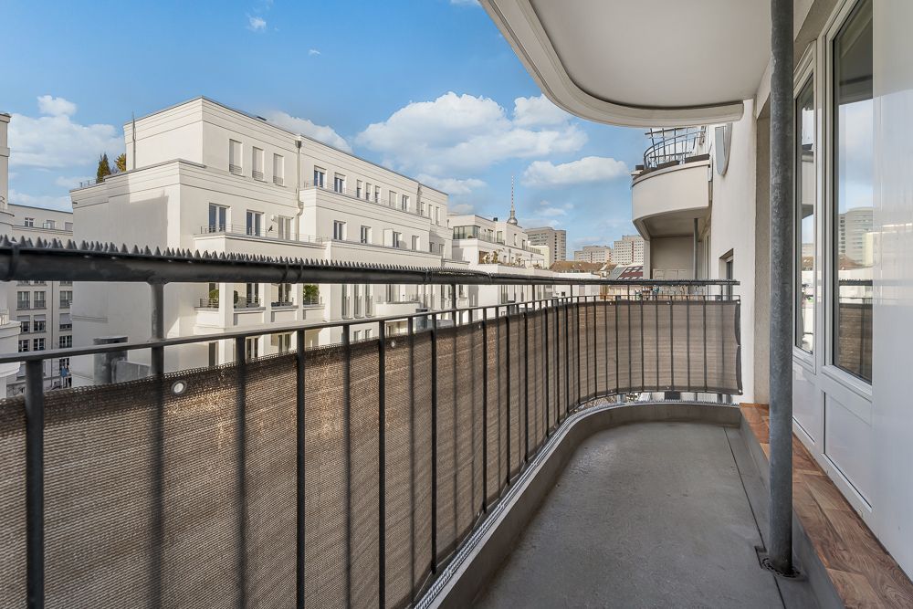 Blick von einem Balkon mit Geländer auf benachbarte Wohngebäude und den Himmel.