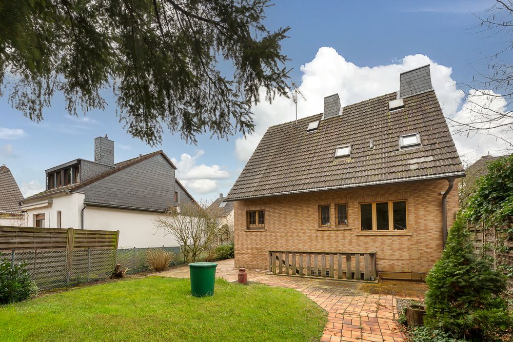 Backstein-Einfamilienhaus mit schrägem Dach, Terrasse und kleinem Garten im Vordergrund.