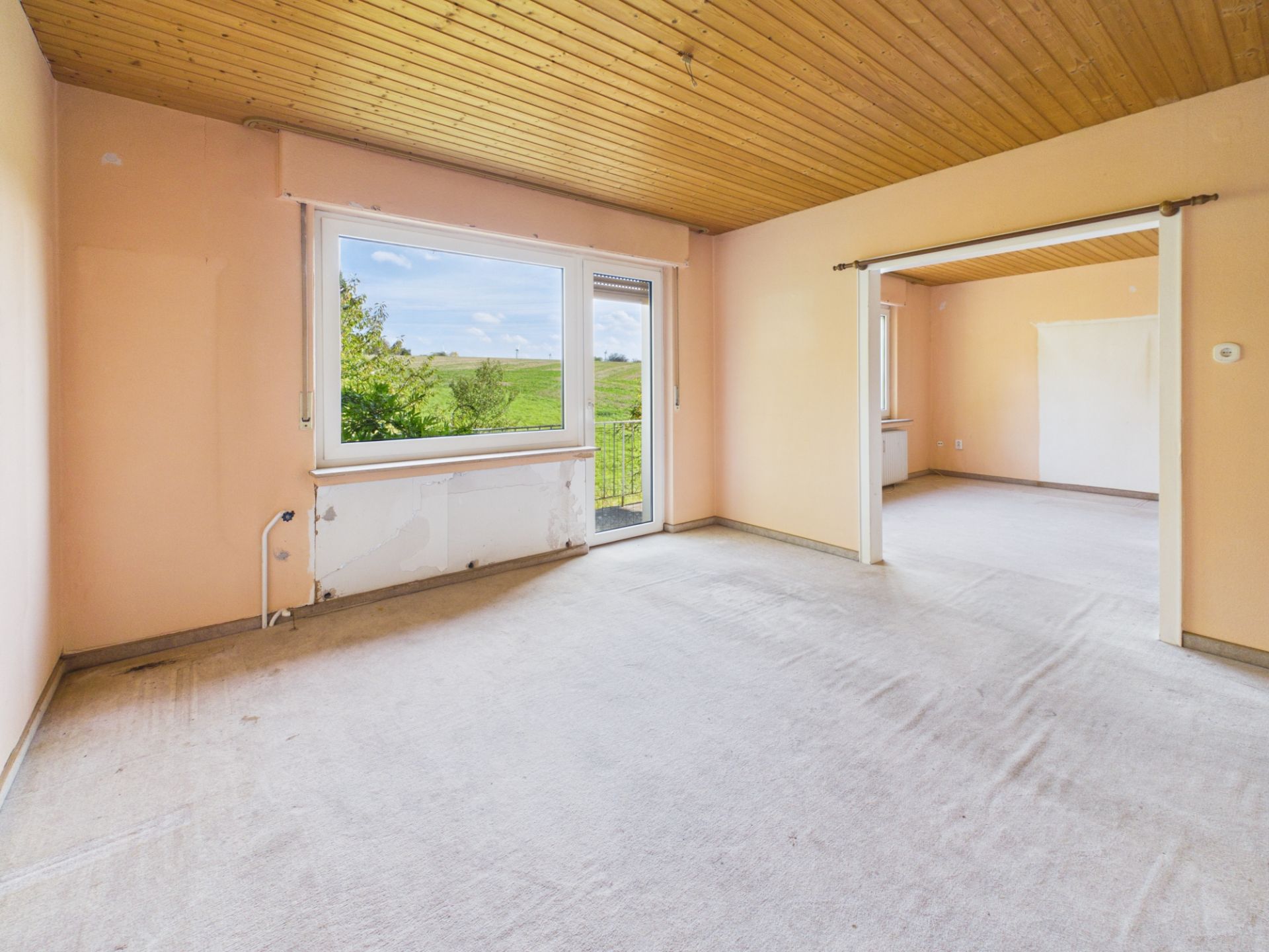Leerer Raum mit großen Fenstern, Blick ins Grüne und Holzdecke.