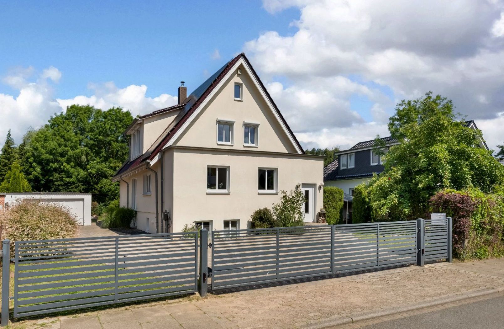 Zweistöckiges Haus mit Satteldach, Vorgarten und modernem Metallzaun bei Tageslicht.