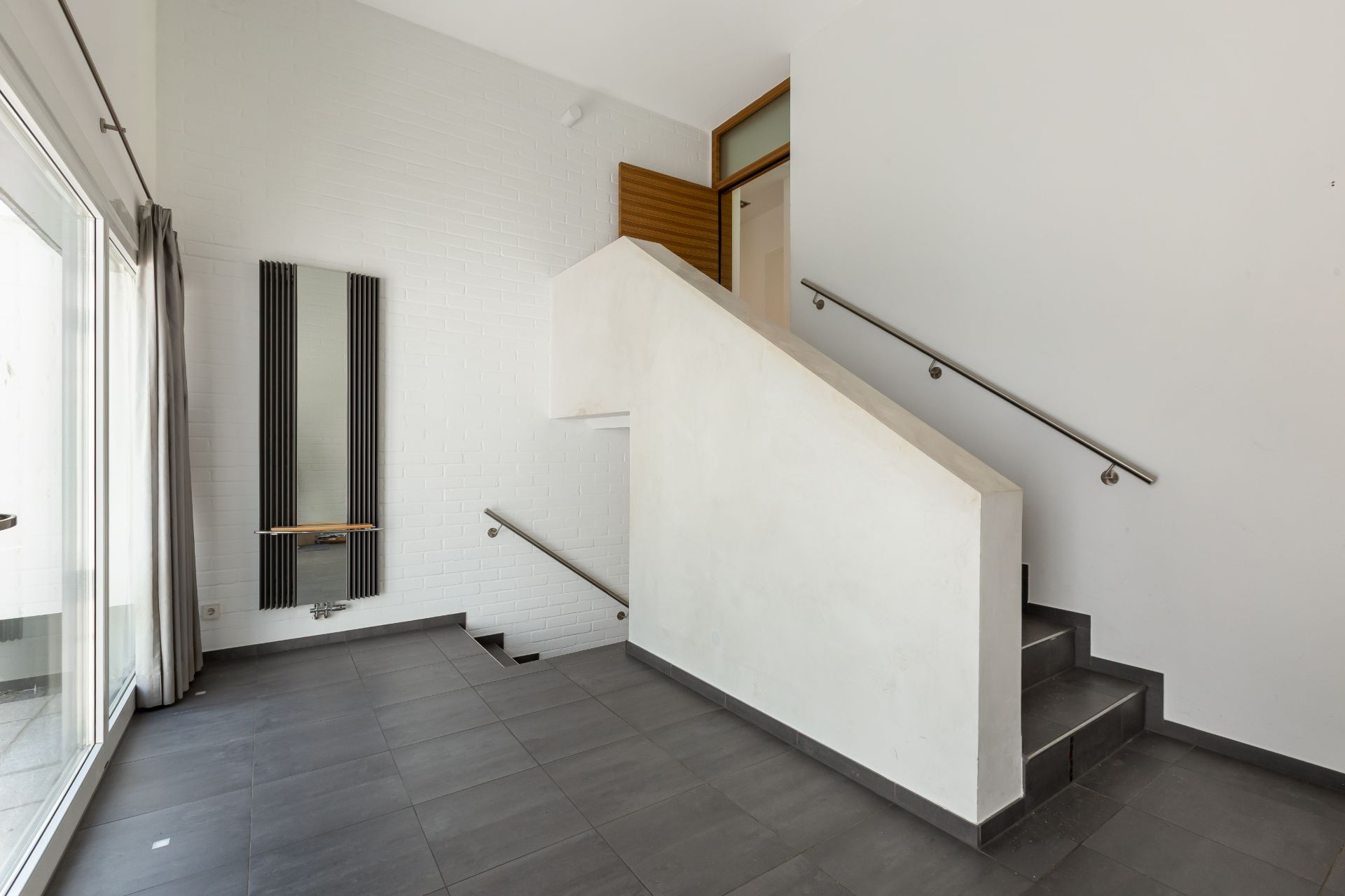 Moderner Flur mit grauem Fliesenboden, Treppe und großem Fenster mit Vorhang.