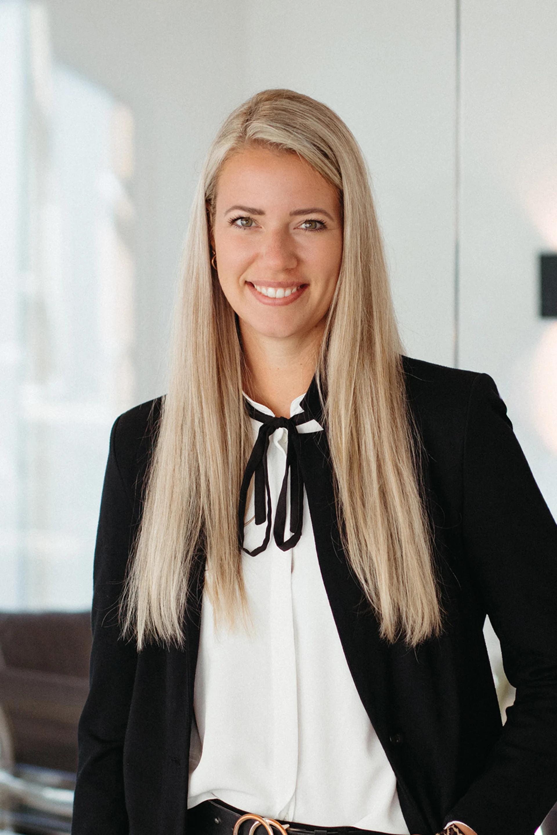 Junge Frau mit langen blonden Haaren lächelt in einem modern eingerichteten Raum.