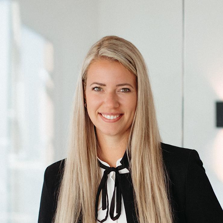 Junge Frau mit langen blonden Haaren lächelt in einem modern eingerichteten Raum.