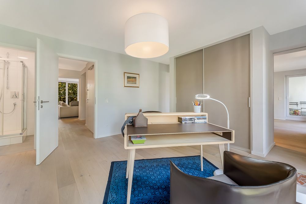 Helles Arbeitszimmer mit Schreibtisch, Stuhl, Teppich und Blick ins Badezimmer.