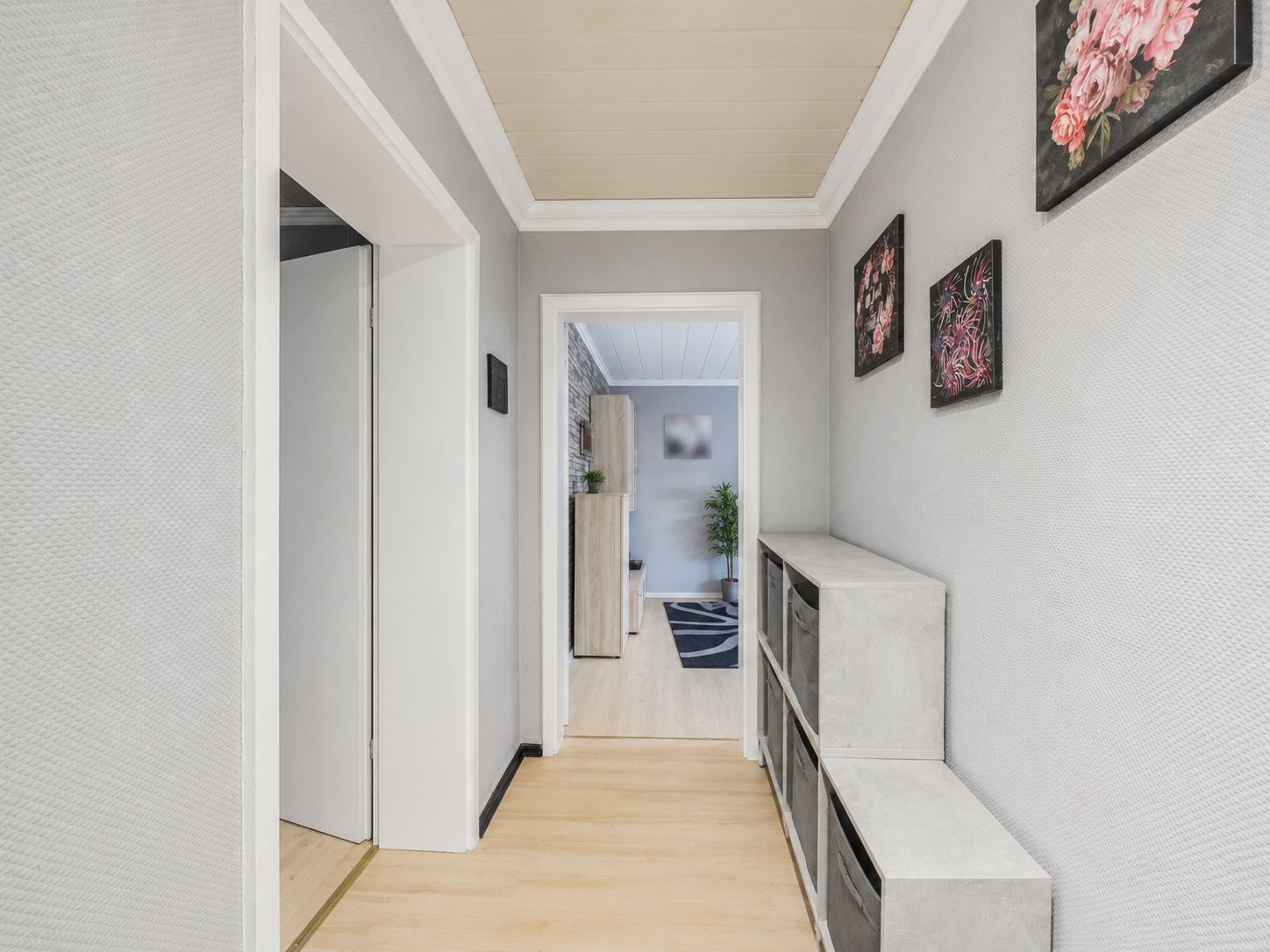 Heller Flur mit grauen Wänden, Kommode und drei Blumenbildern an der Wand.