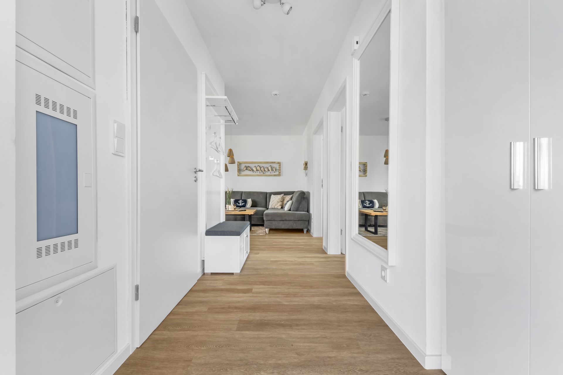 Heller Flur mit Holzboden, Spiegel und Blick auf ein Wohnzimmer mit grauem Sofa.