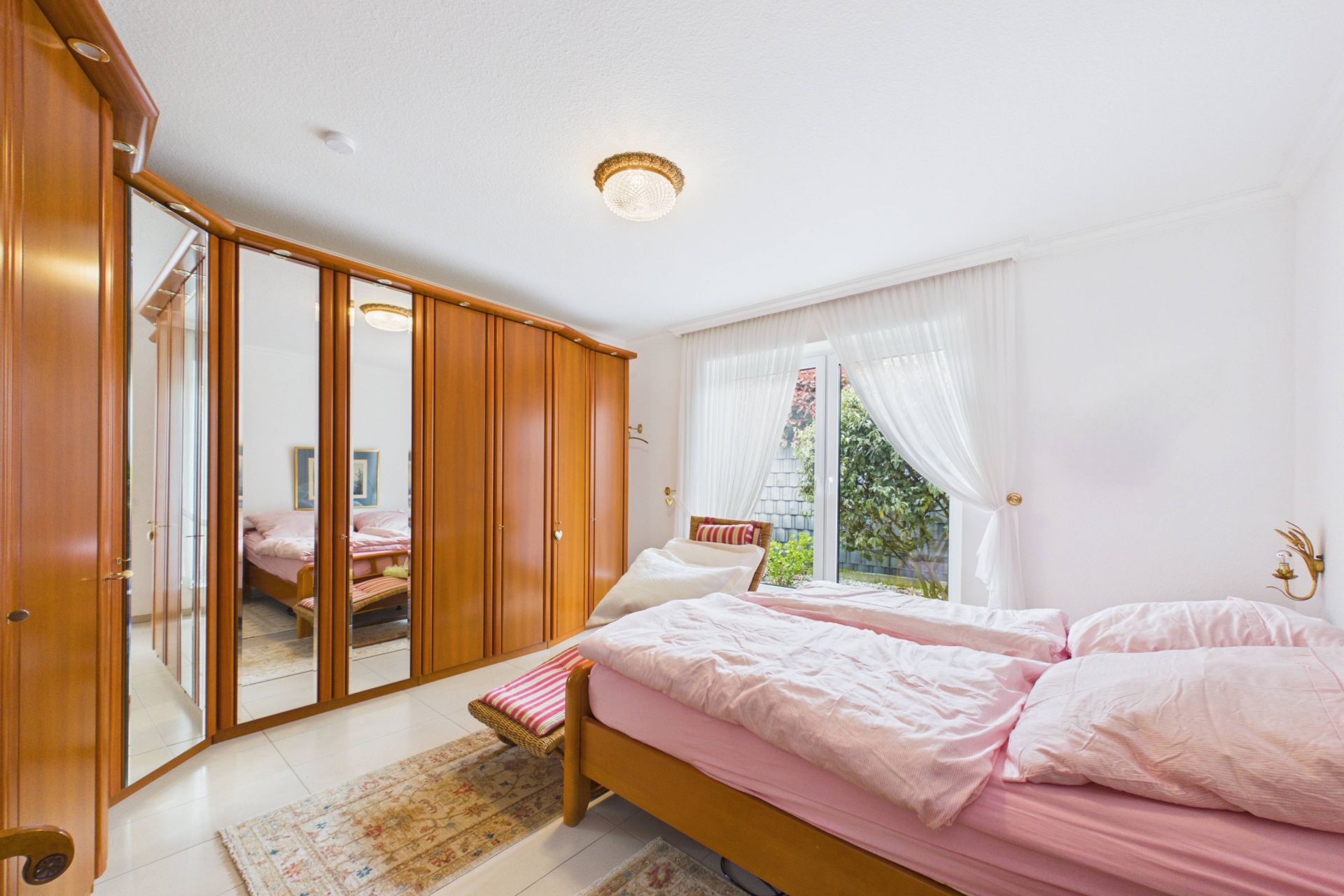 Helles Schlafzimmer mit großem Holzkleiderschrank, Doppelbett und Fenster mit Blick auf den Garten.