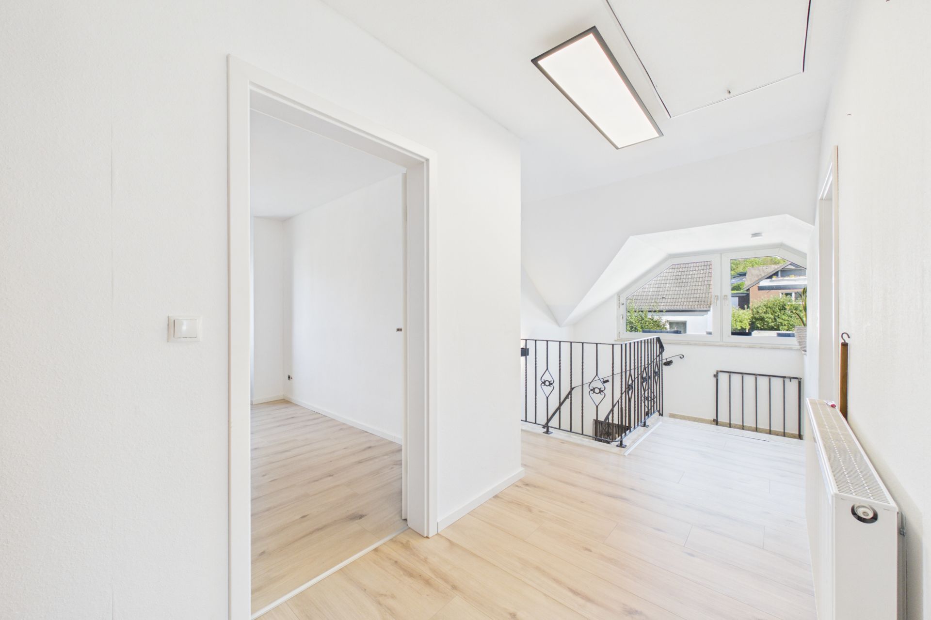 Heller Flur mit Holzfußboden und Geländer, Fenster mit Blick nach draußen.