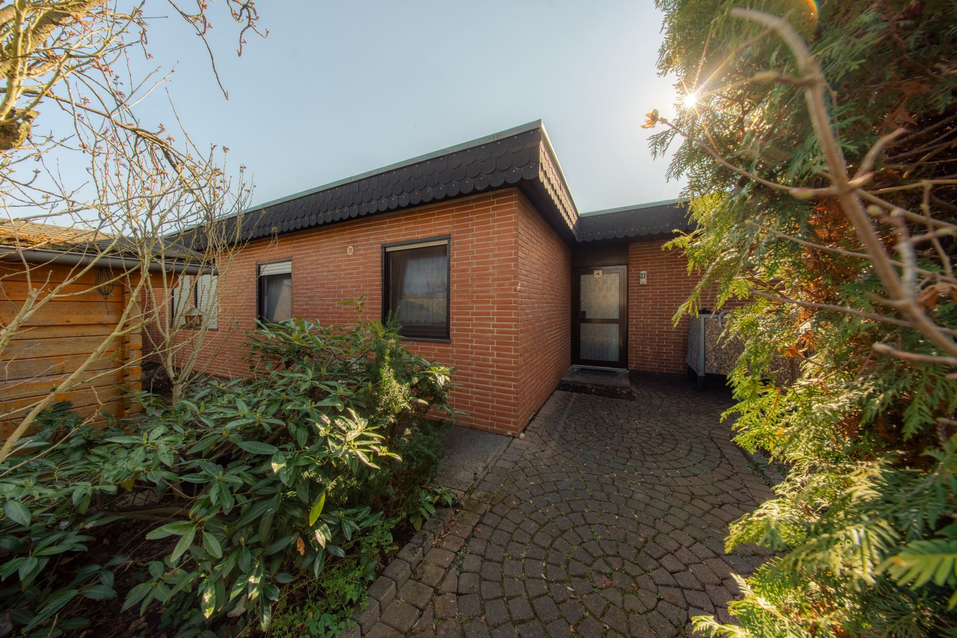 Einfamilienhaus mit roter Klinkerfassade, Pflasterweg und umgebenden Büschen.