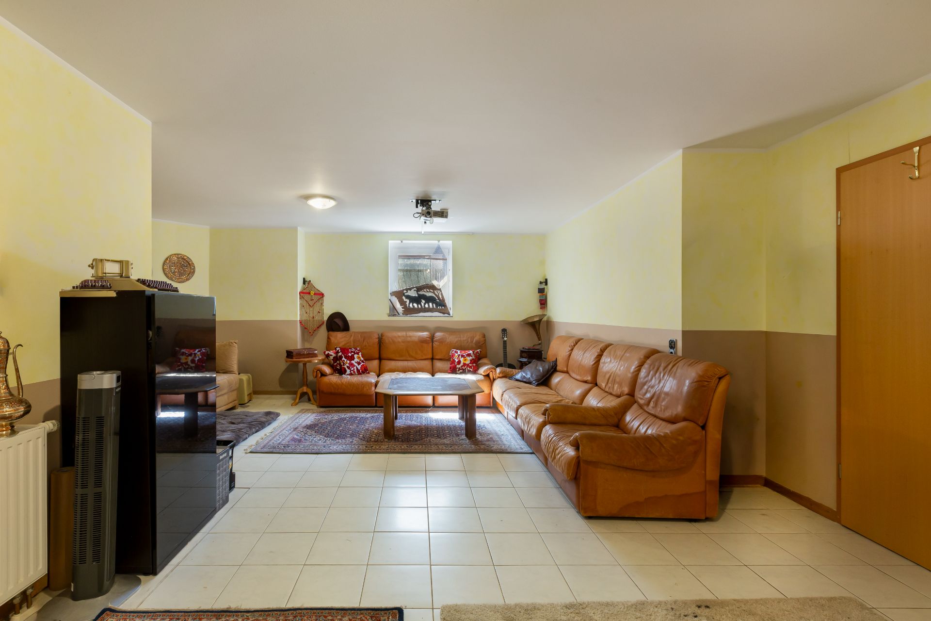 Wohnzimmer mit braunen Ledersofas, Couchtisch und Teppichen auf hellem Fliesenboden.