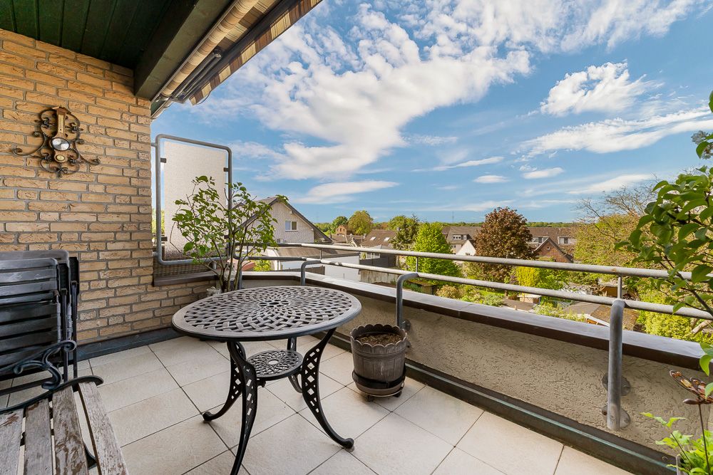 Balkon mit Metalltisch, Stuhl, Pflanzen und Blick auf Dächer und grüne Bäume.