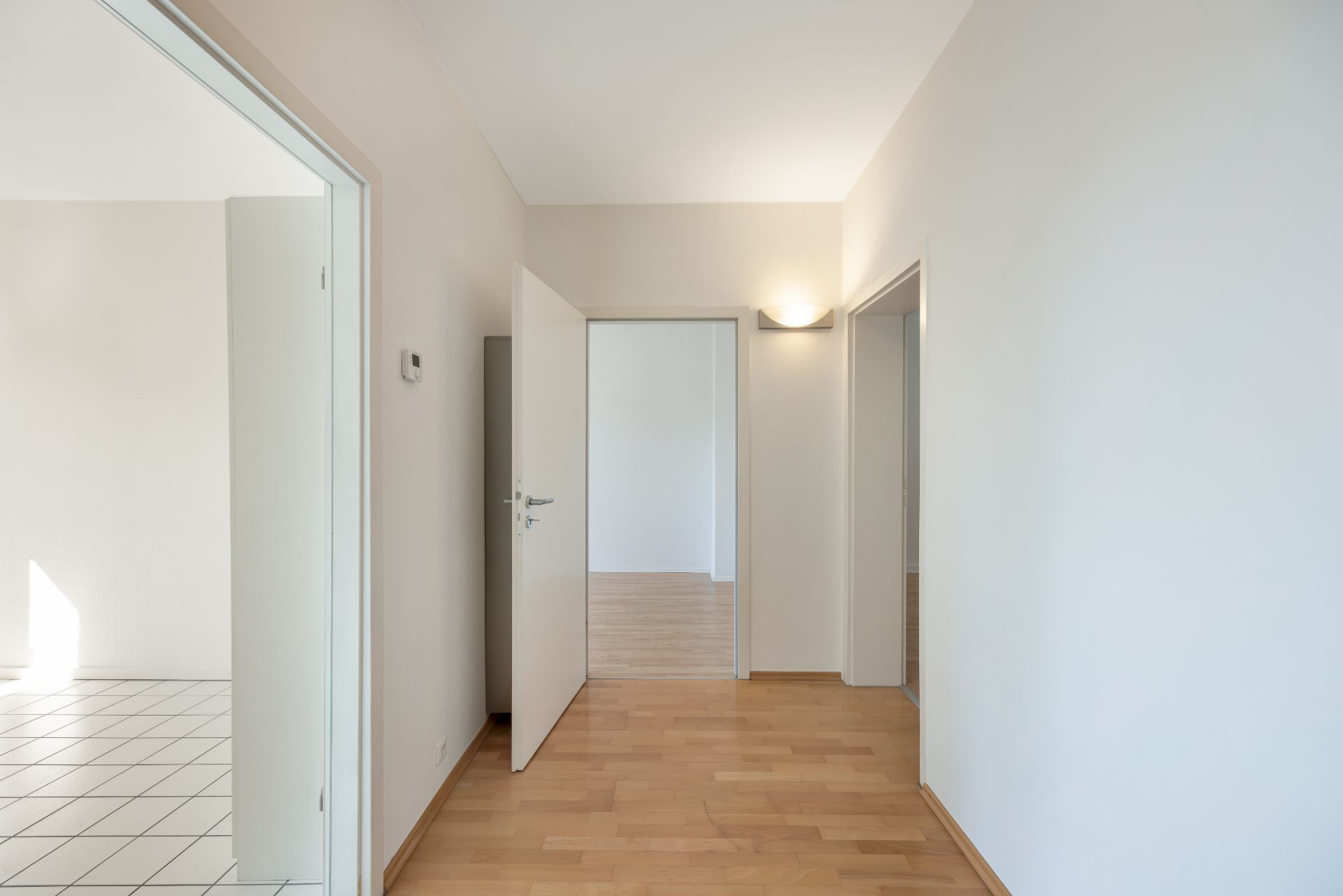 Heller Flur mit Holzboden, mehrere offene Türen zu angrenzenden Räumen, weiße Wände.