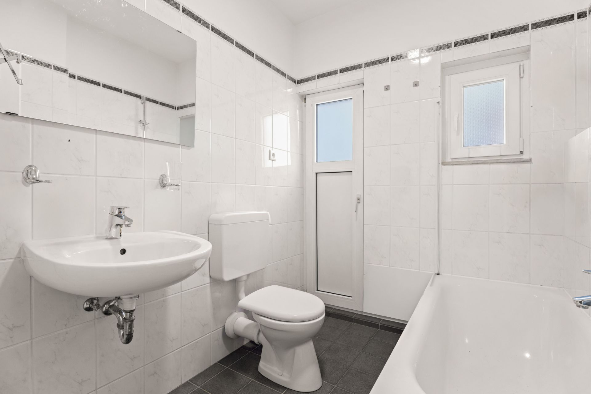 Modernes Badezimmer mit Waschbecken, Toilette, Badewanne und zwei Fenstern.