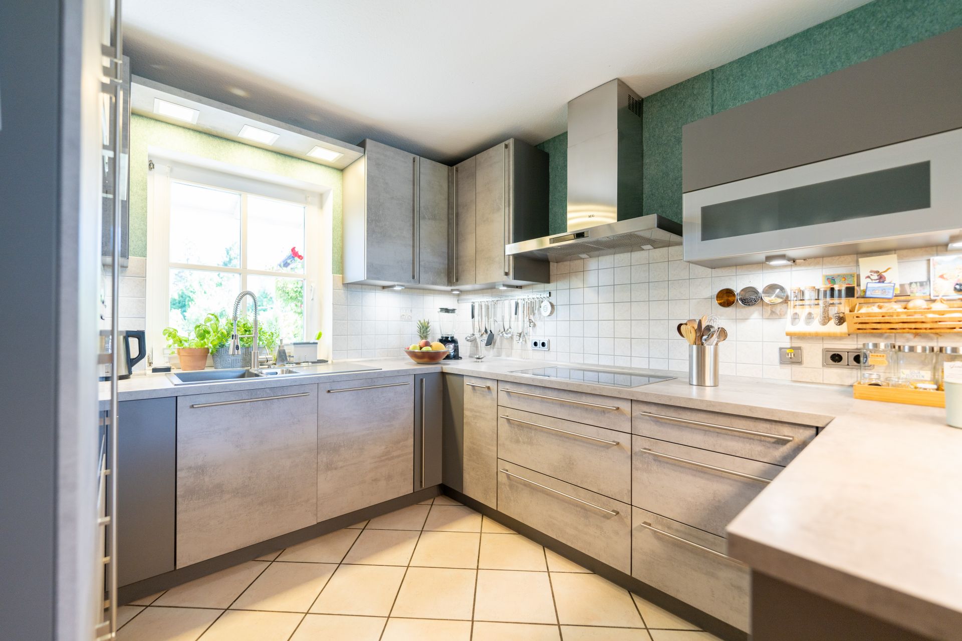 Moderne Küche mit grauen Schränken, großem Fenster und Küchenutensilien an der Wand.