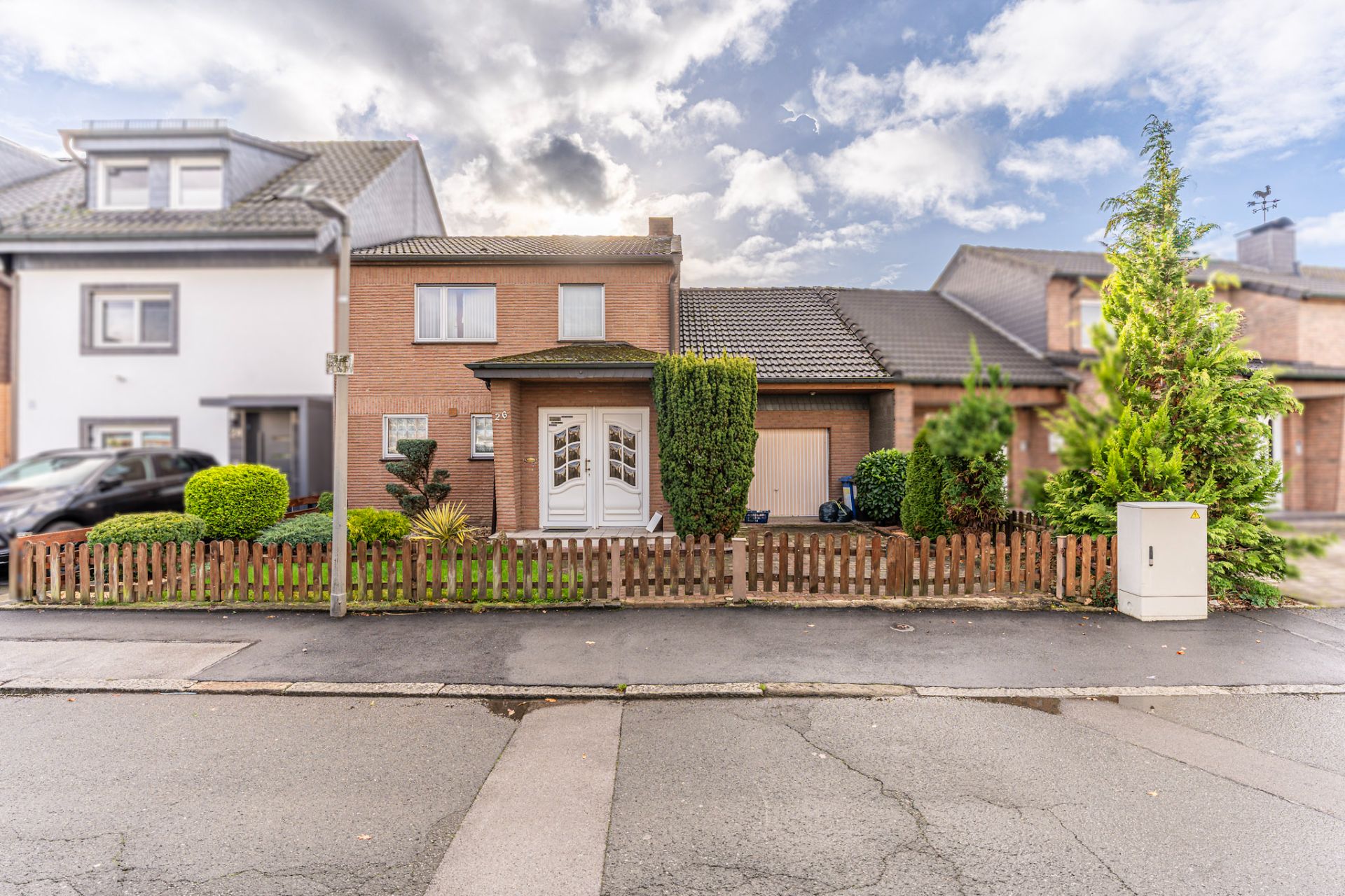 Zweistöckiges Wohnhaus mit Vorgarten, Holzzaun und einer Garage rechts neben dem Eingang.