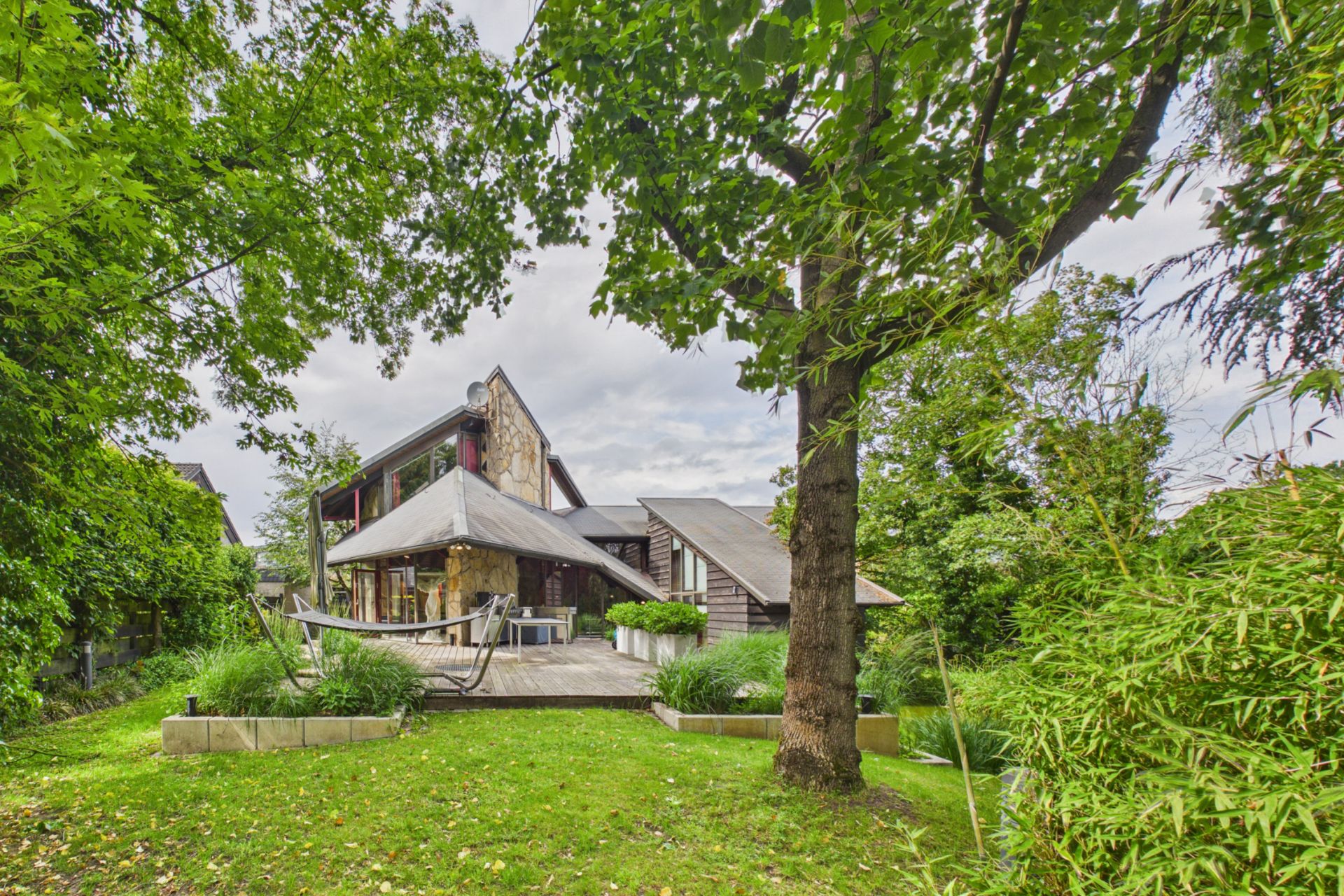 Modernes Wohnhaus mit großer Terrasse, Hängematte, Bäumen und Garten.