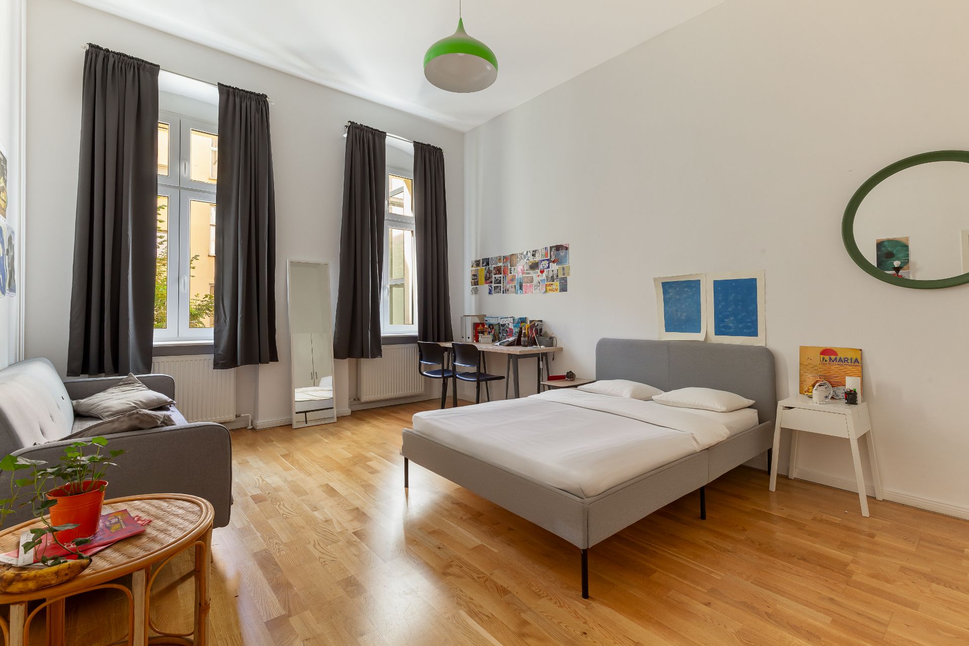 Helles Schlafzimmer mit Doppelbett, Sofa, Schreibtisch, großem Fenster und Holzboden.
