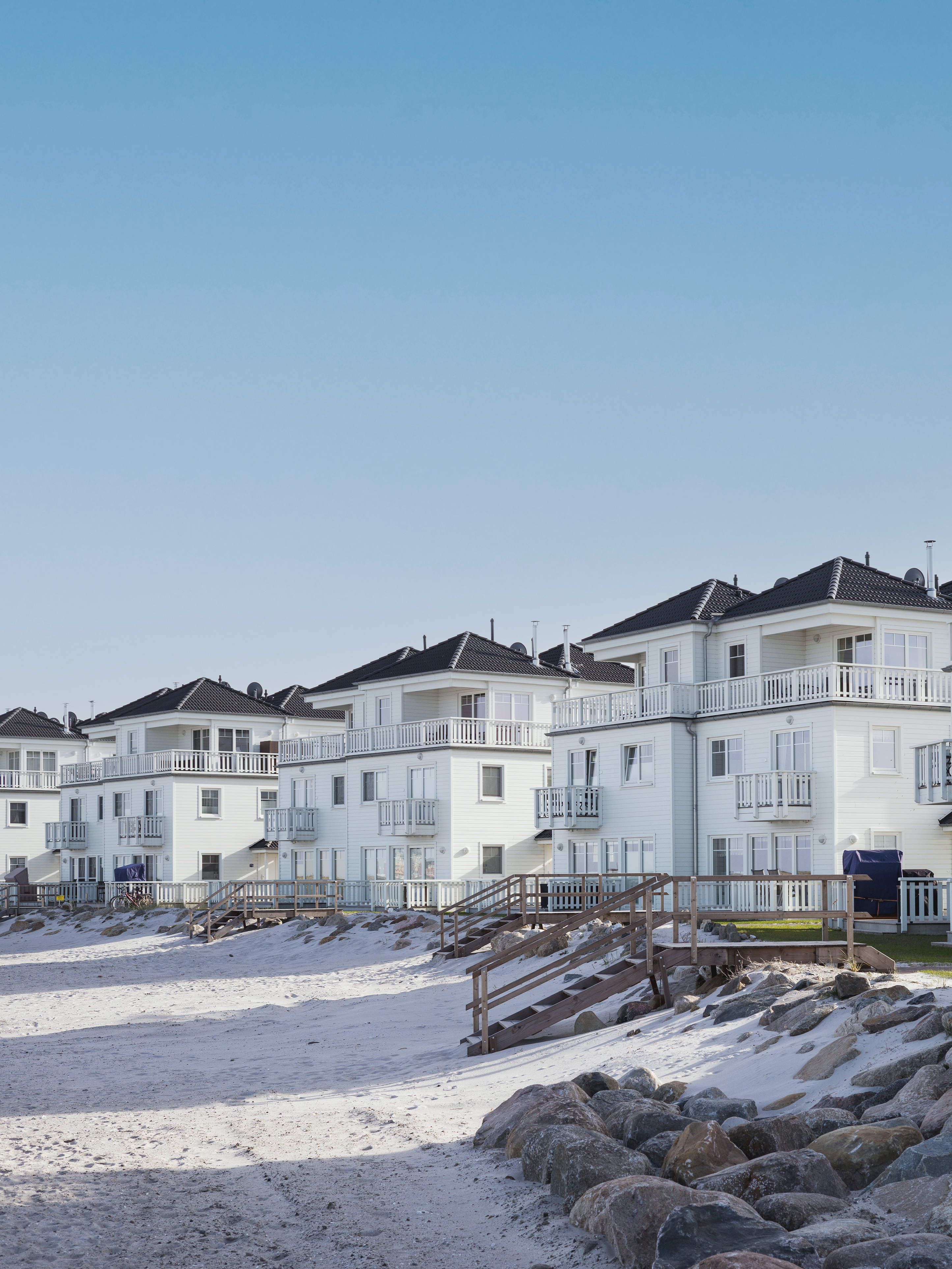 Mehrstöckige weiße Wohnhäuser mit Balkonen direkt am Sandstrand und Felsen.