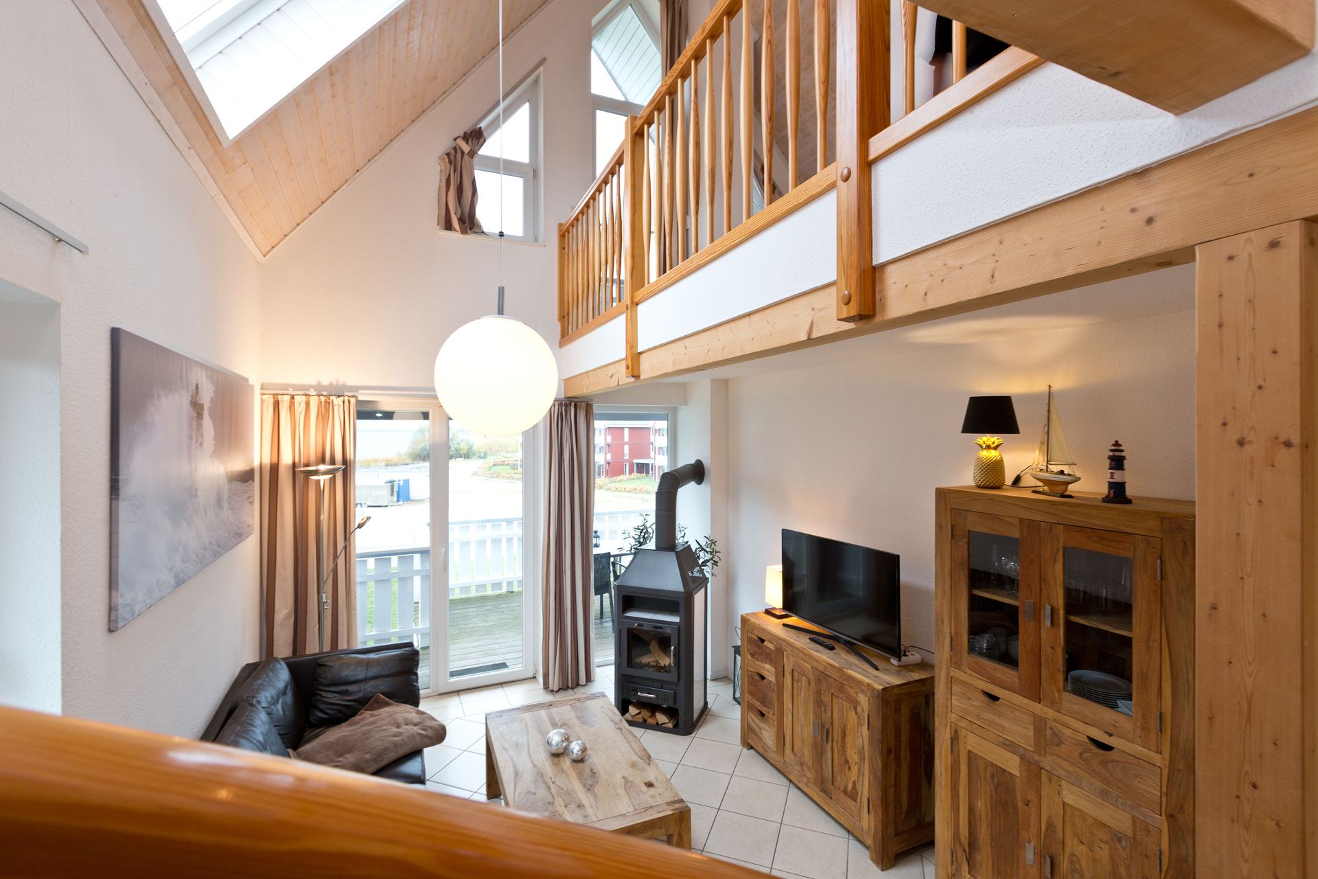 Wohnzimmer mit Holzdecke, Sofa, Couchtisch, Fernseher, Kamin und einer offenen Galerie.