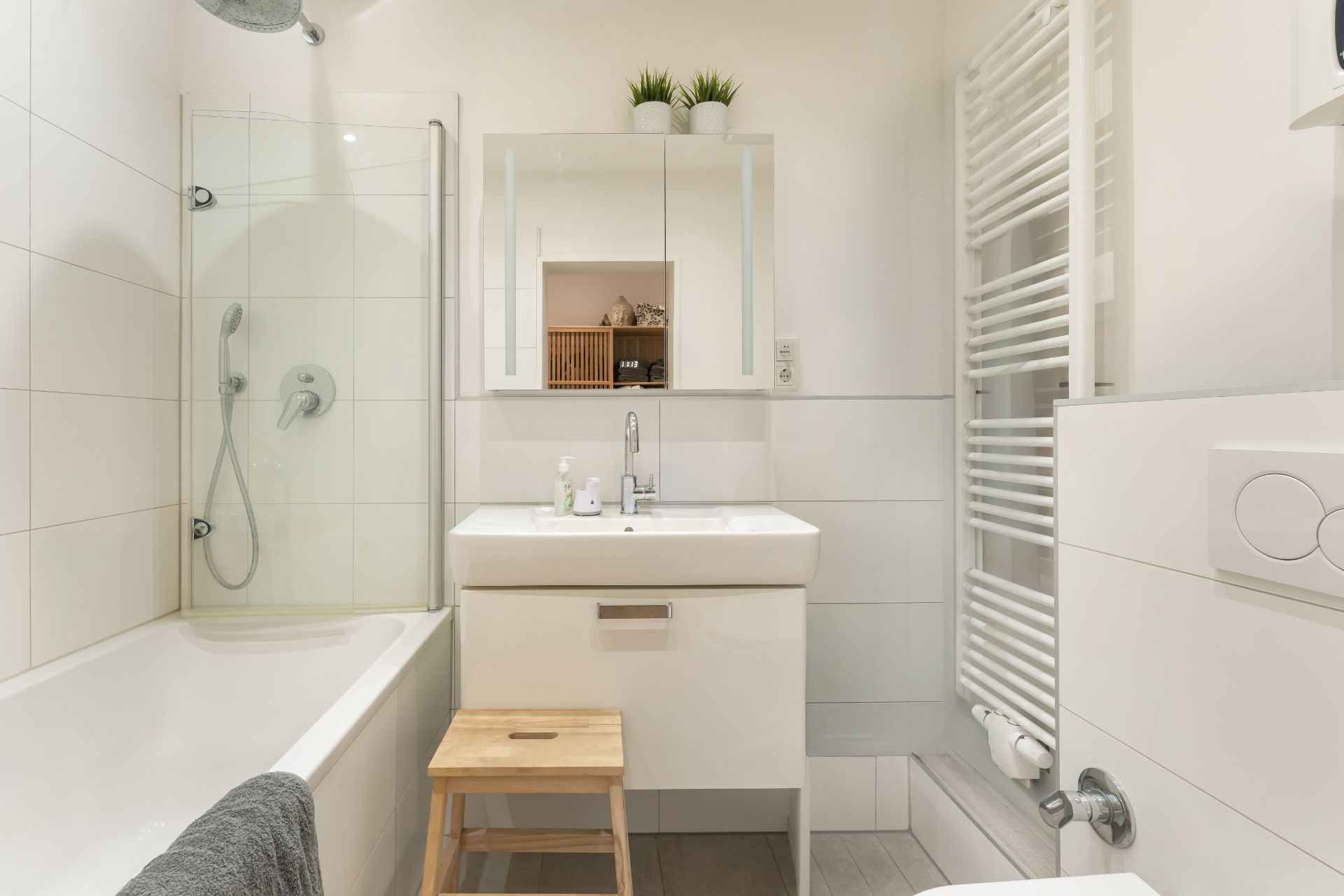 Modernes Badezimmer mit Badewanne, Waschbecken, Spiegel, Handtuchheizkörper und Holzschemel.