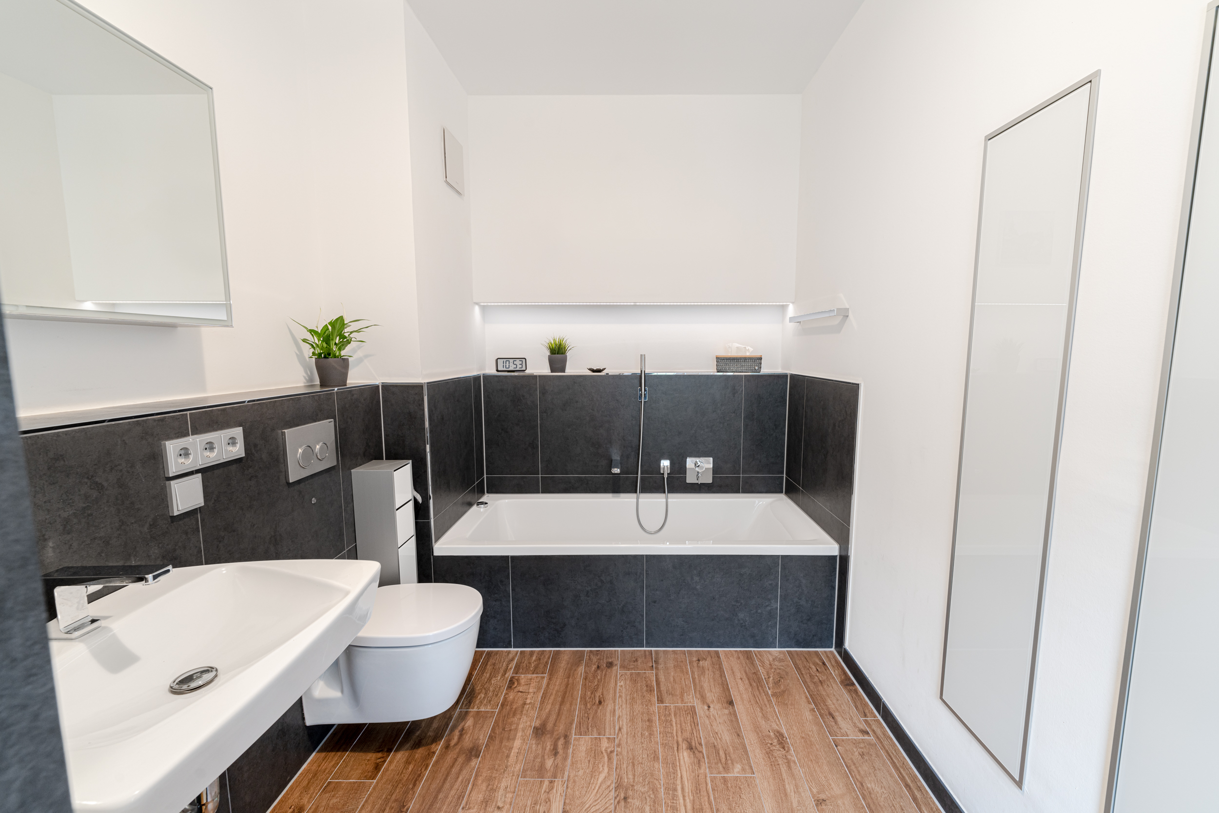 Modernes Badezimmer mit Badewanne, Waschbecken, WC und Holzoptik-Fliesenboden.