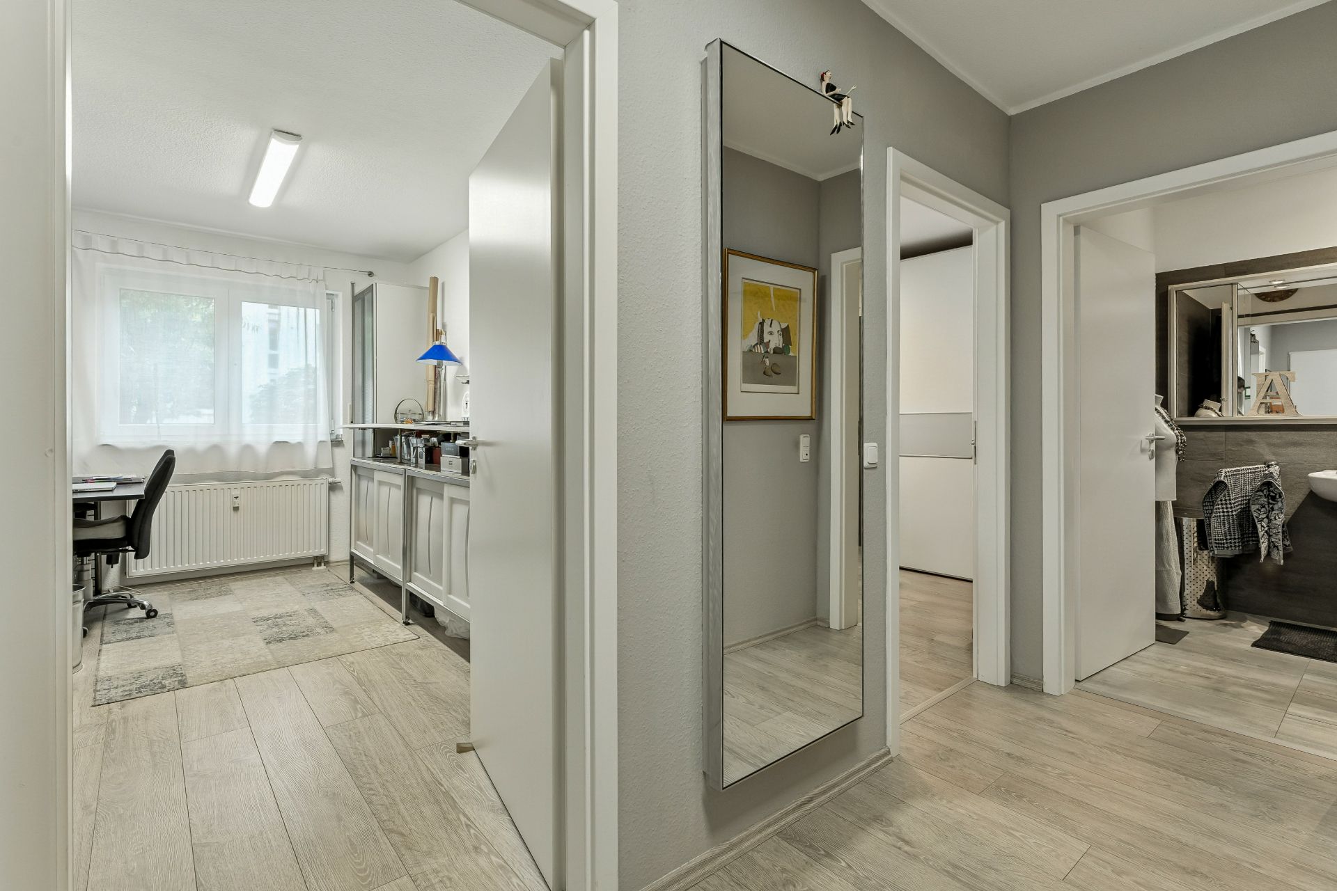 Heller Flur mit Spiegel, mehreren Türen und Blick in ein Arbeitszimmer sowie ein Badezimmer.