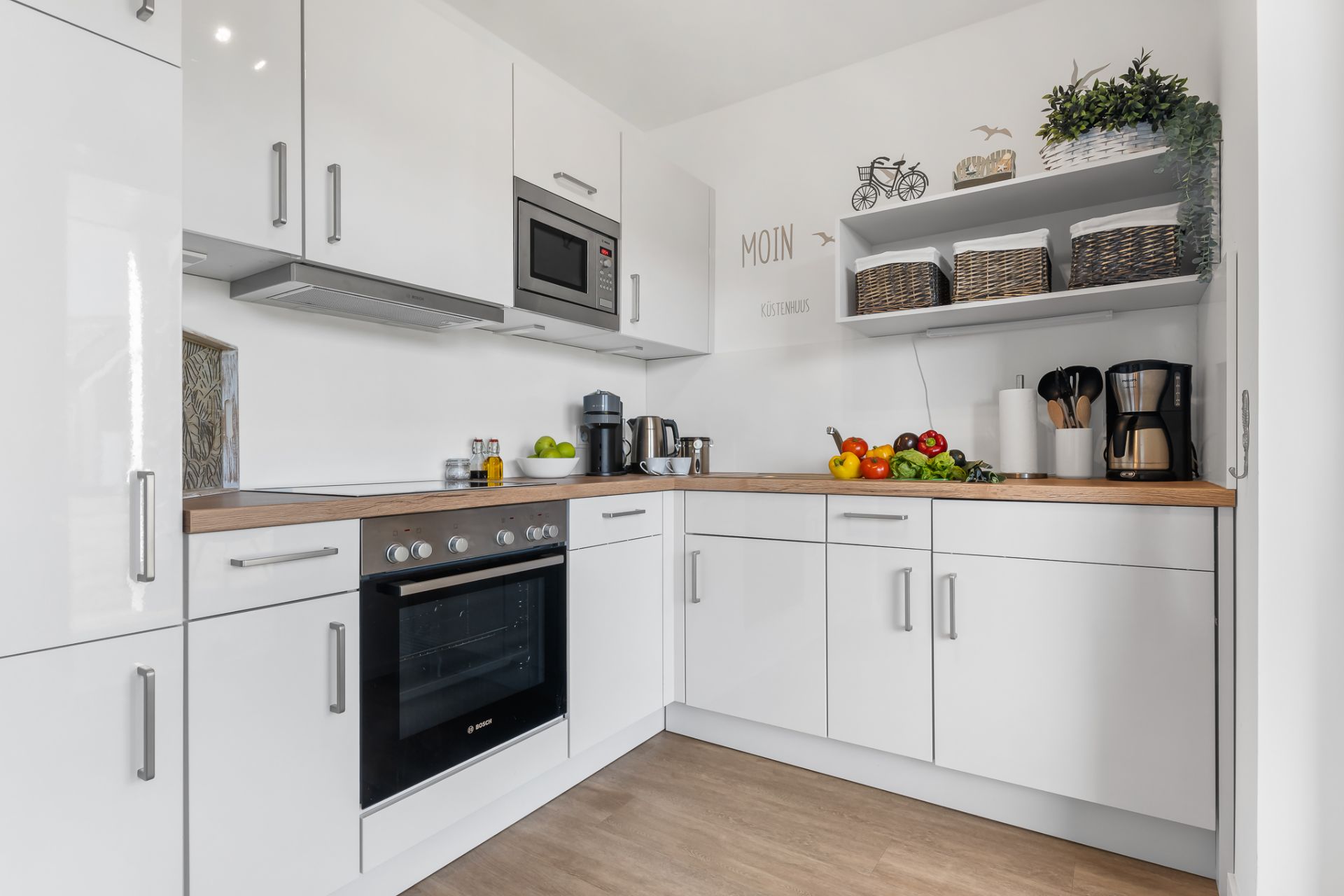 Moderne weiße Einbauküche mit Holzarbeitsplatte und Obst auf der Theke.