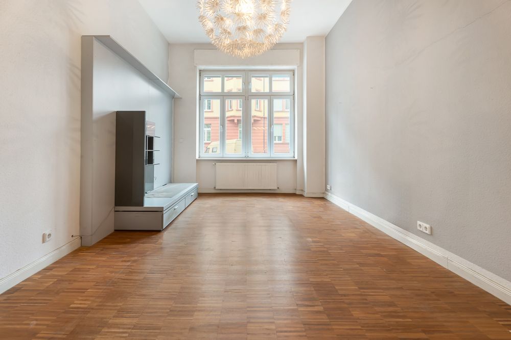 Leeres Wohnzimmer mit Holzfußboden, großem Fenster und moderner Deckenleuchte.