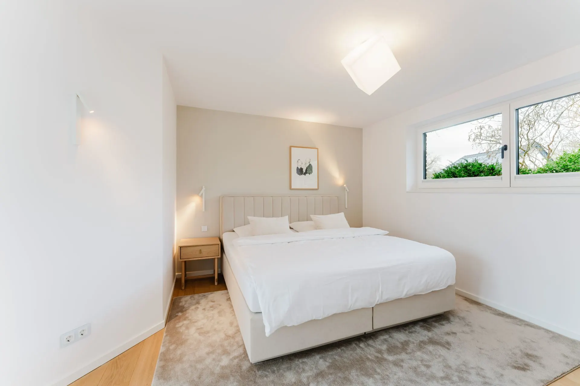 Helles Schlafzimmer mit Doppelbett, Nachttisch und großem Fenster mit Blick ins Grüne.