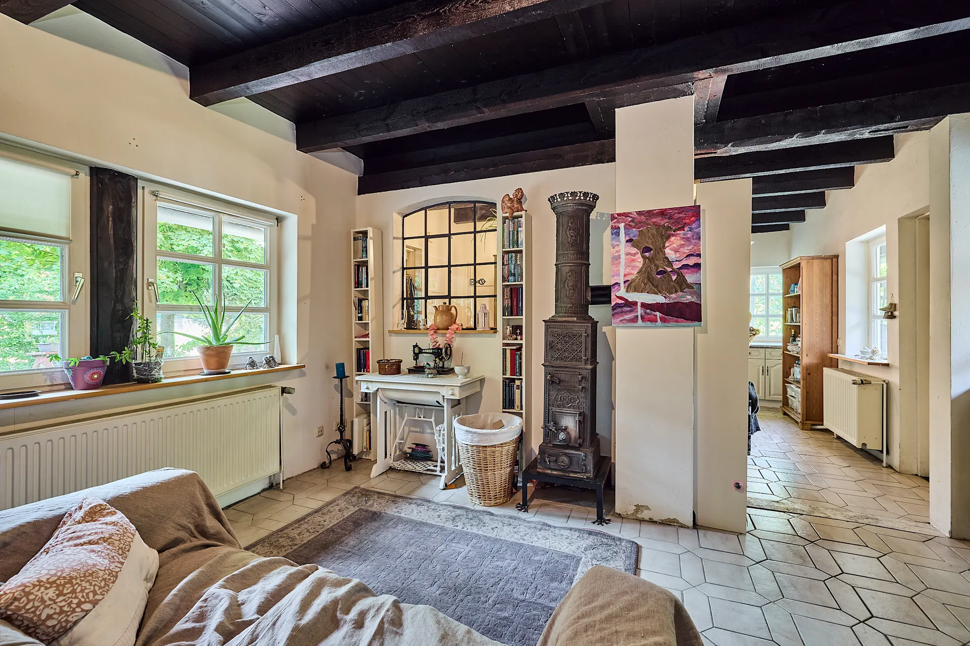 Gemütliches Wohnzimmer mit Sofa, Kaminofen, Schreibtisch, großen Fenstern und Pflanzen.