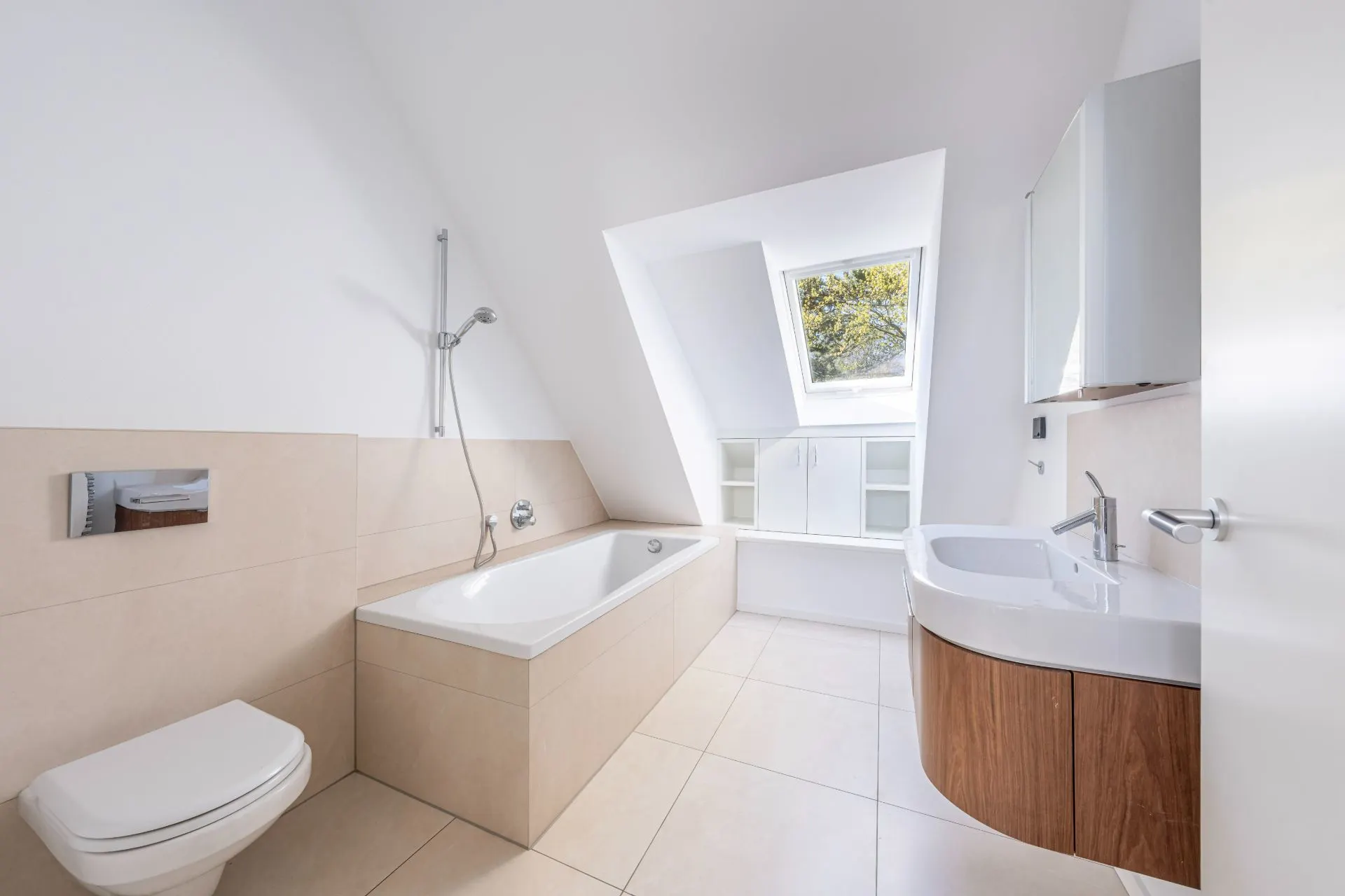 Helles Bad mit Badewanne, Wandtoilette, Waschbecken und großem Fenster im Dachgeschoss.