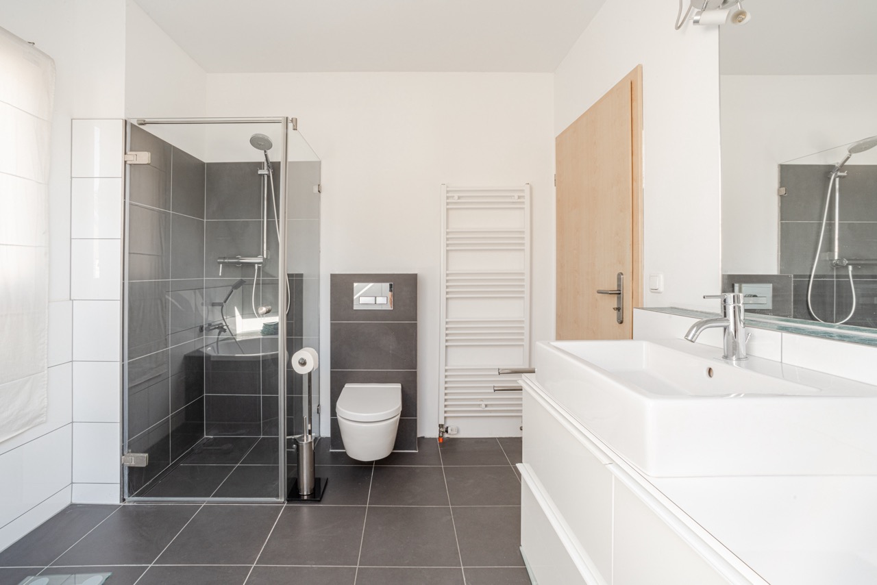 Modernes Badezimmer mit ebenerdiger Dusche, Wandtoilette und Doppelwaschbecken.