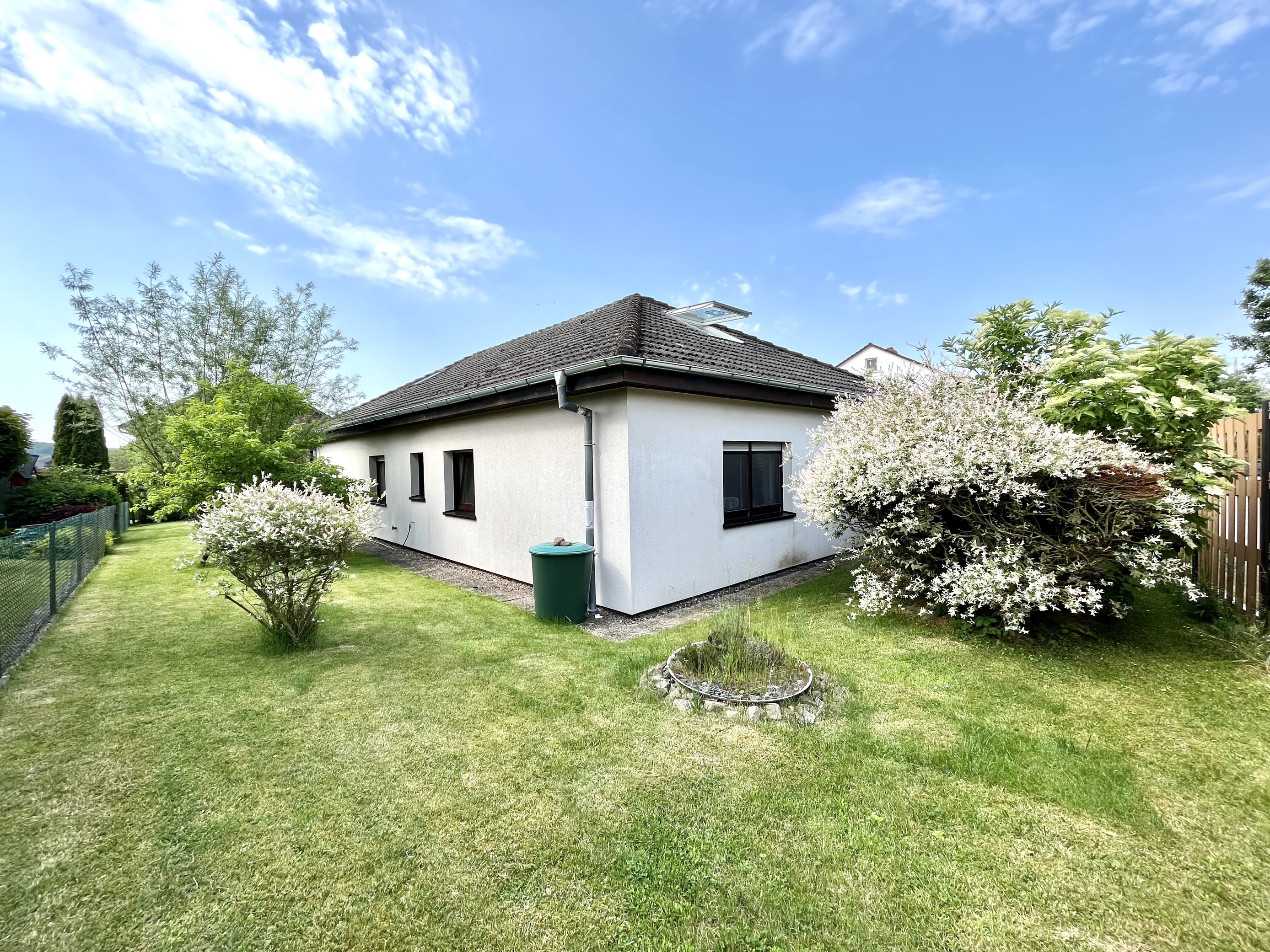Einfamilienhaus mit Garten, Rasen, Büschen und Bäumen unter blauem Himmel.