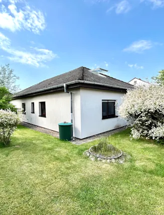 Einfamilienhaus mit Garten, Rasen, Büschen und Bäumen unter blauem Himmel.