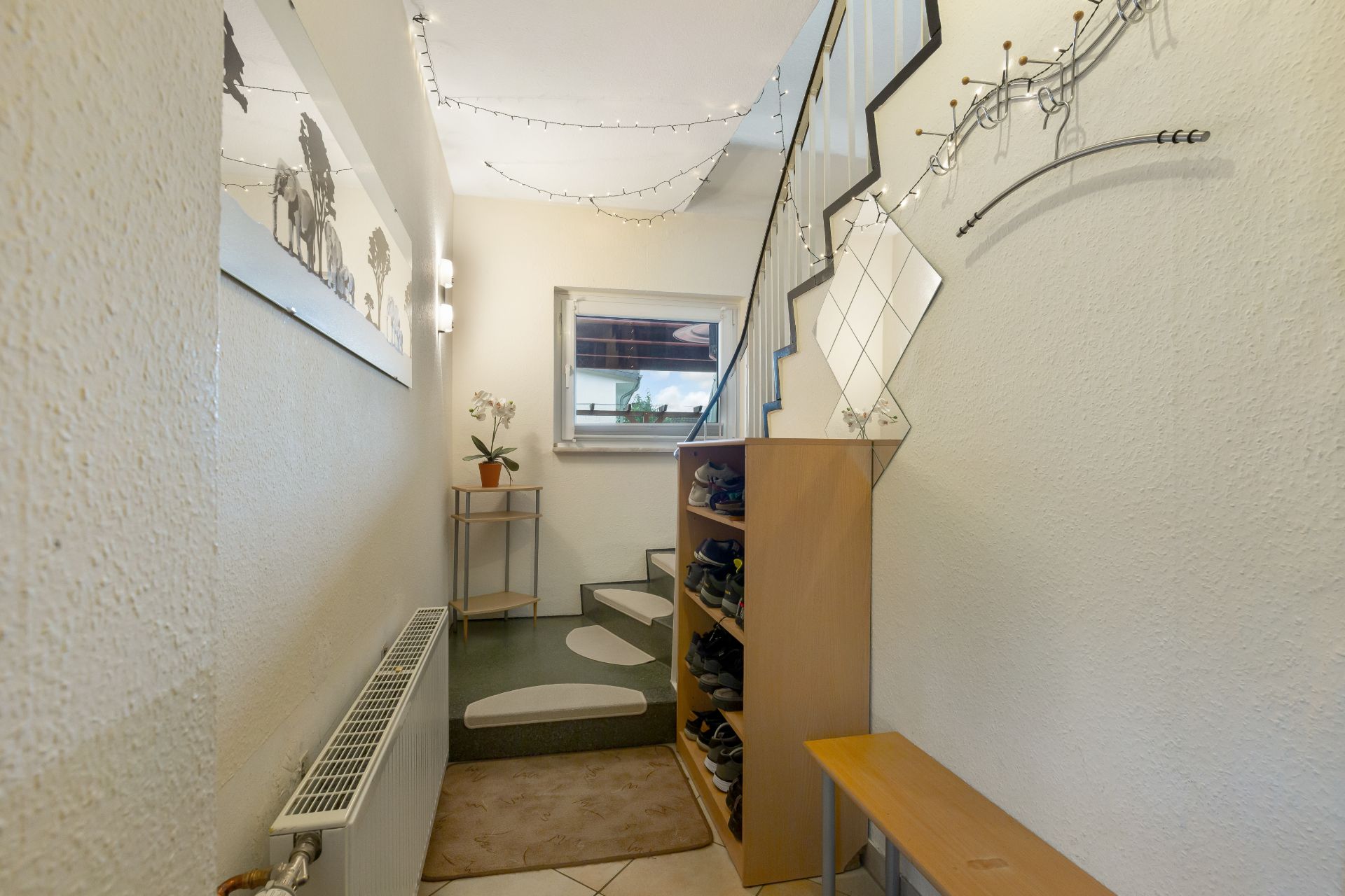 Heller Flur mit Schuhregal, Sitzbank, Spiegel und Treppe, dekoriert mit Lichterkette.