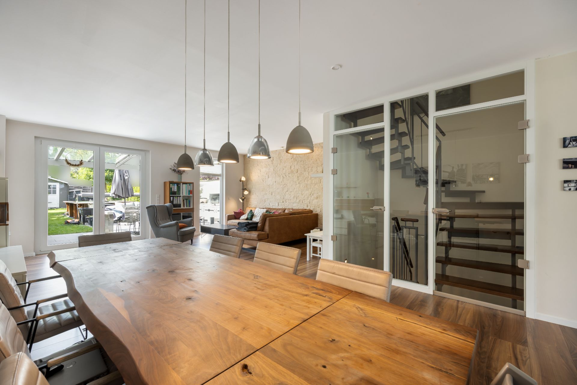 Essbereich mit Holztisch, Stühlen, Hängelampen, Wohnzimmer und Blick in den Garten.