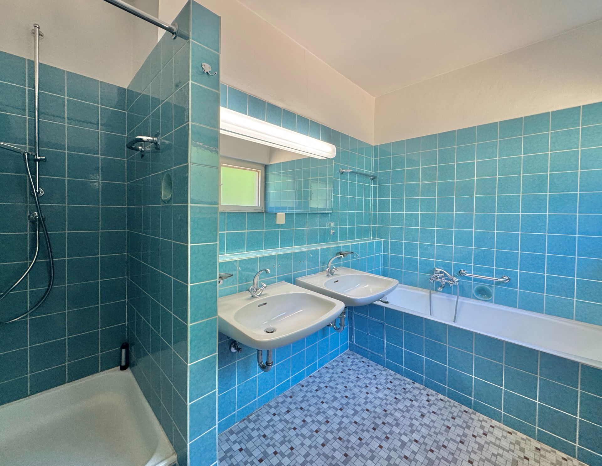 Helles Bad mit blauen Fliesen, zwei Waschbecken, Badewanne und Dusche.