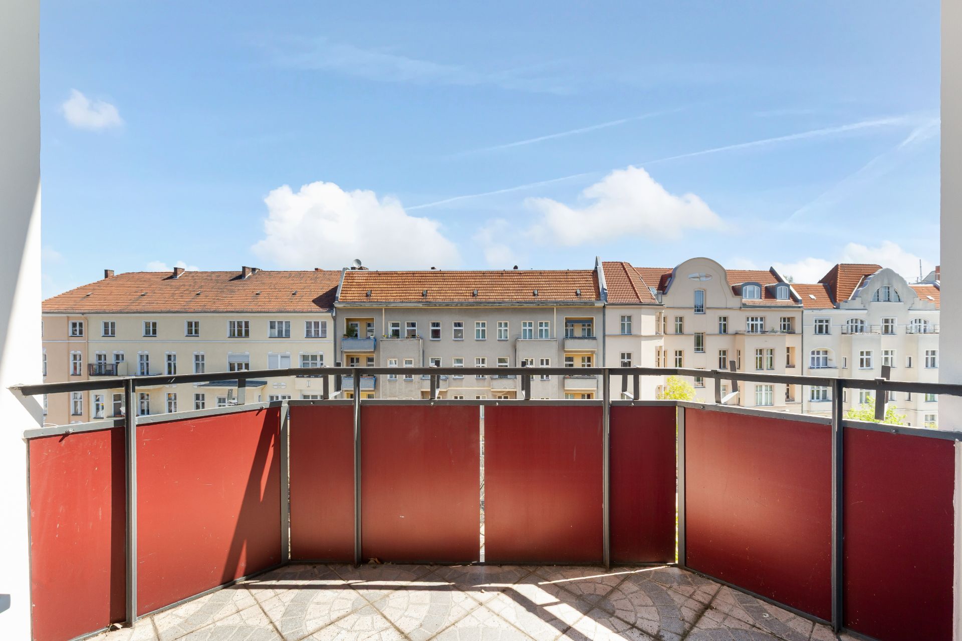 Balkon mit roter Brüstung und Blick auf gegenüberliegende Wohnhäuser.