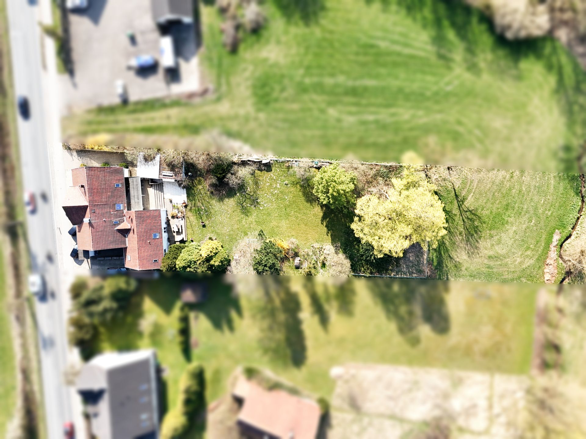 Luftaufnahme eines Wohnhauses mit großem Garten und Bäumen entlang einer Straße.