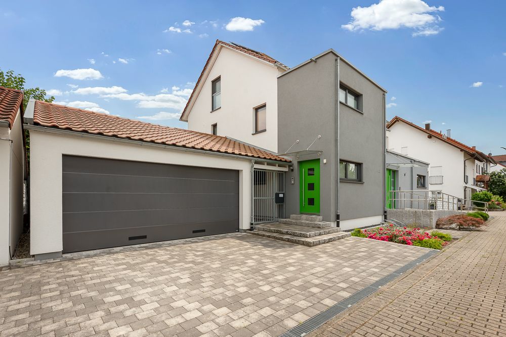 Modernes Wohnhaus mit grauer Garage, grünem Eingang und Vorgarten mit Blumen.